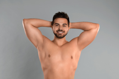 Photo of Young man showing hairless armpits after epilation procedure on grey background