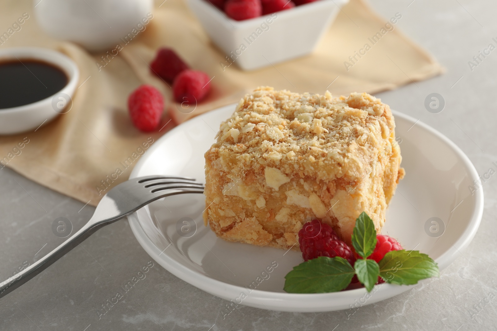 Photo of Piece of delicious Napoleon cake, raspberries and fork on beige table, closeup