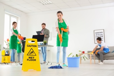 WET FLOOR sign and team of professional janitors in office