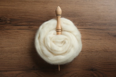 Photo of Soft white wool with spindle on wooden table, top view