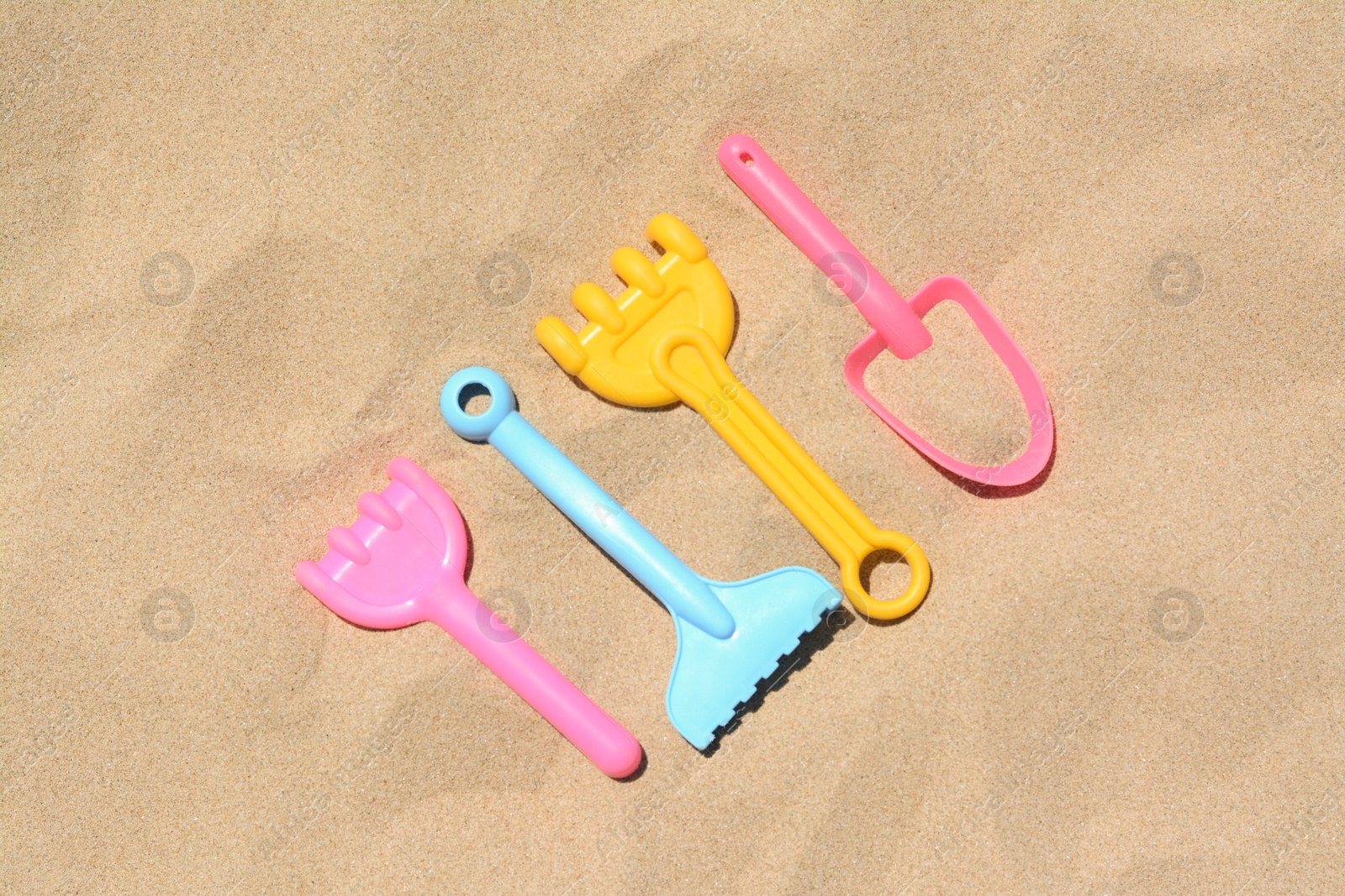 Photo of Bright plastic rakes and shovel on sand, flat lay. Beach toys