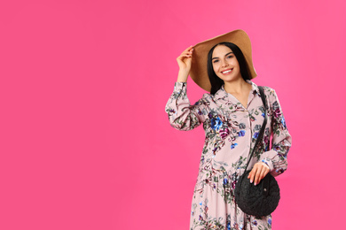 Photo of Young woman wearing floral print dress and straw hat on pink background. Space for text