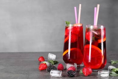 Photo of Delicious refreshing sangria, ice cubes and berries on grey table, space for text