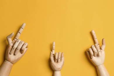 Wooden mannequin hands on yellow background, flat lay