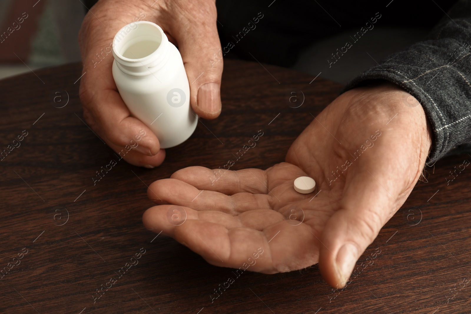 Photo of Senior man holding bottle and pill at table, closeup of hands