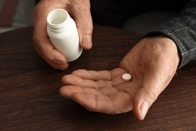 Senior man holding bottle and pill at table, closeup of hands