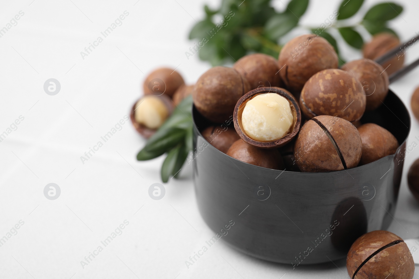 Photo of Tasty organic Macadamia nuts in small saucepan on white table, closeup. Space for text