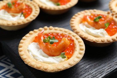 Delicious canapes with shrimps, red caviar and cream cheese on dark table, closeup