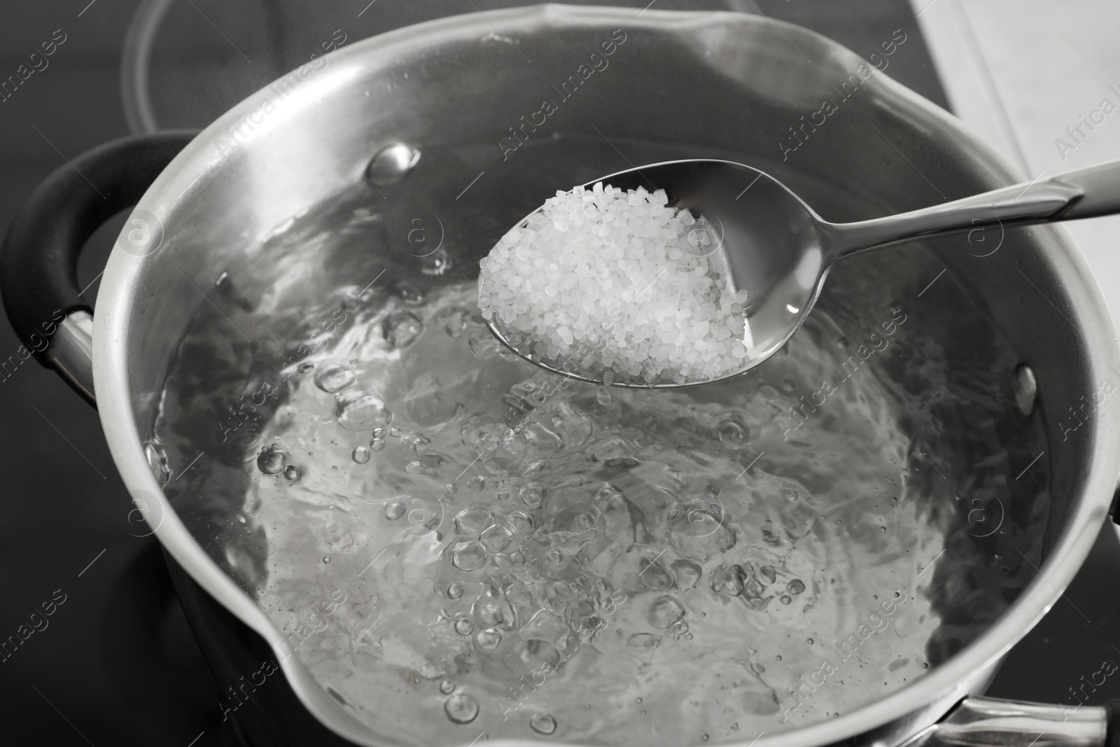 Photo of Salting boiling water in pot on stove, closeup