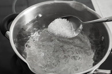 Salting boiling water in pot on stove, closeup