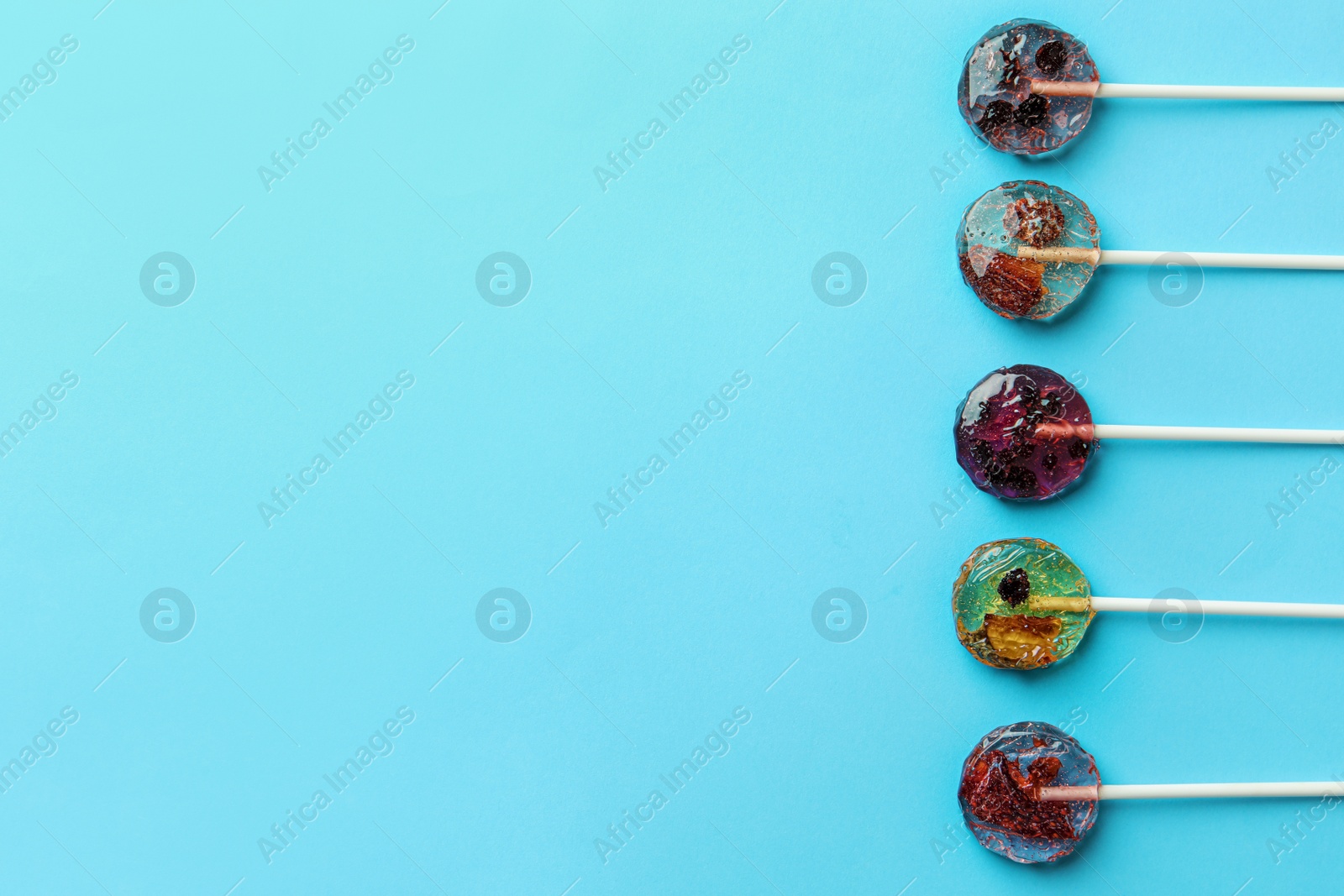 Photo of Sweet colorful lollipops with berries on light blue background, flat lay. Space for text