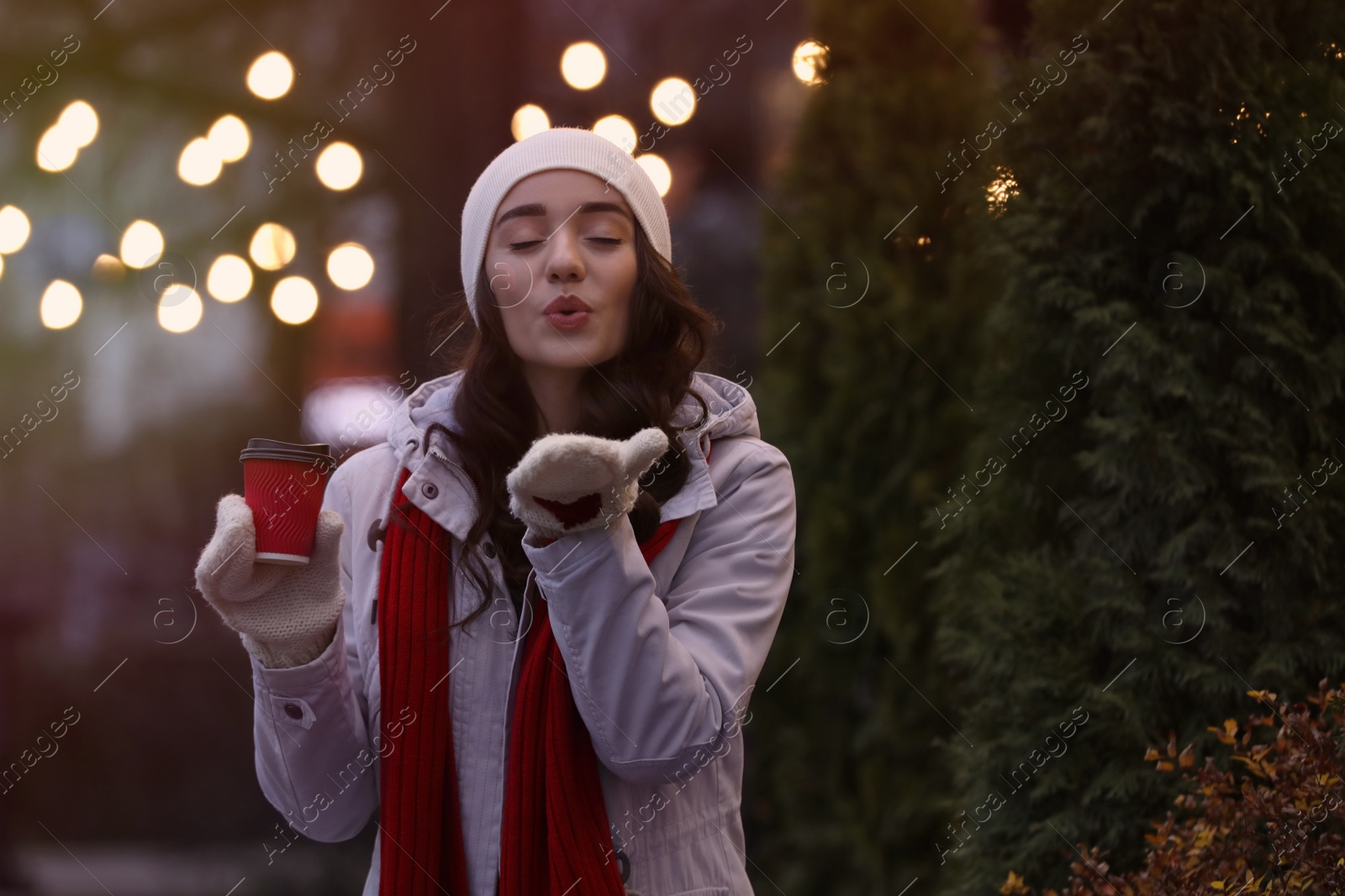 Photo of Happy young woman with cup of drink on city street in evening. Christmas celebration