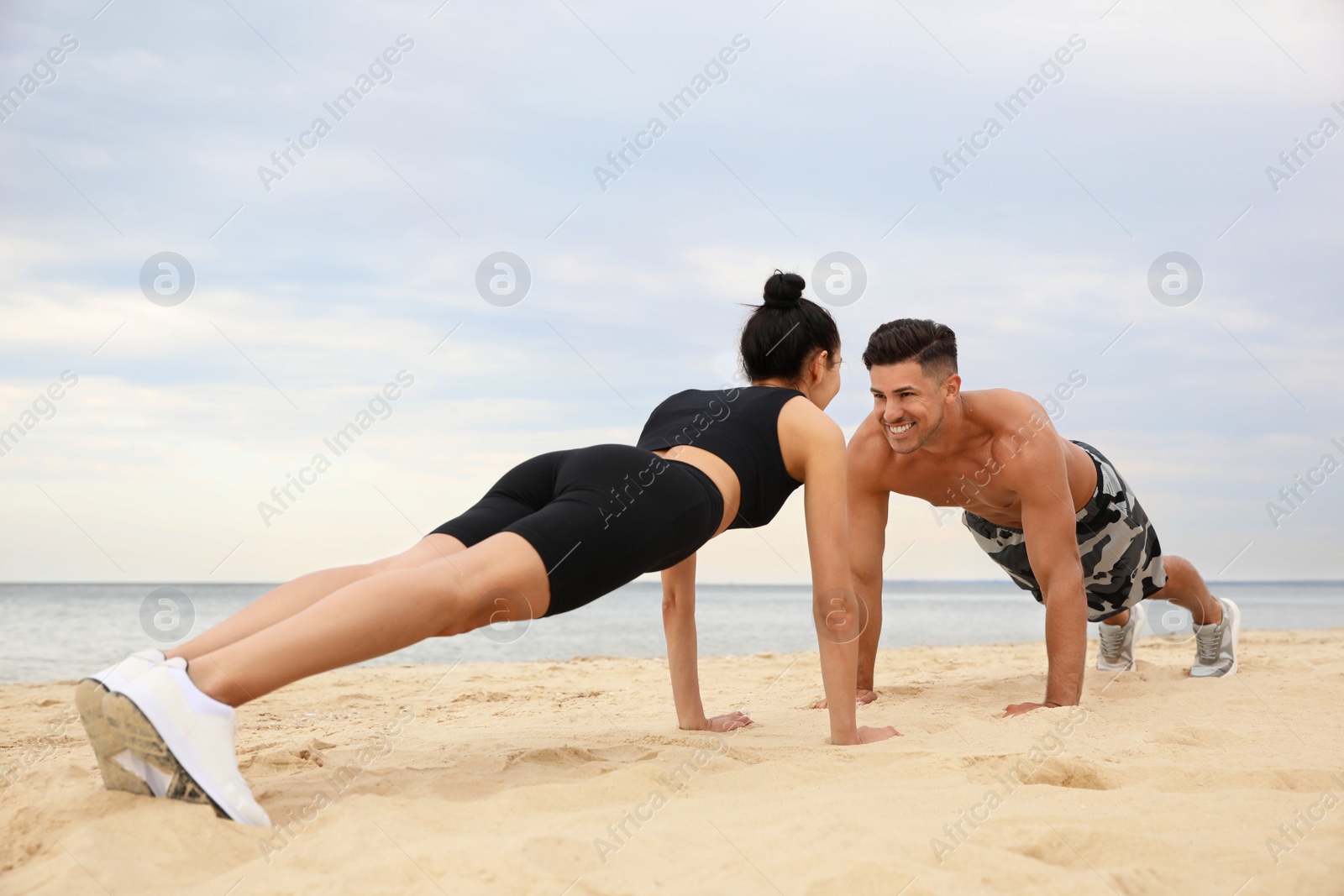 Photo of Couple doing exercise together on beach. Body training