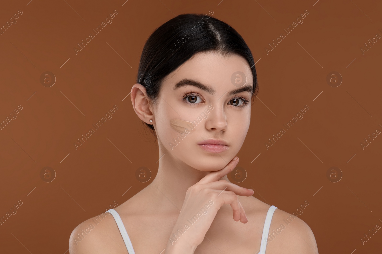 Photo of Teenage girl with swatch of foundation on face against brown background