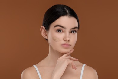 Teenage girl with swatch of foundation on face against brown background