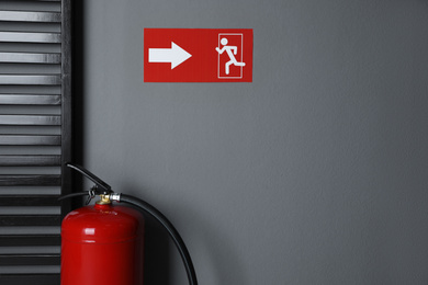 Photo of Fire extinguisher and emergency exit sign indoors. Space for text