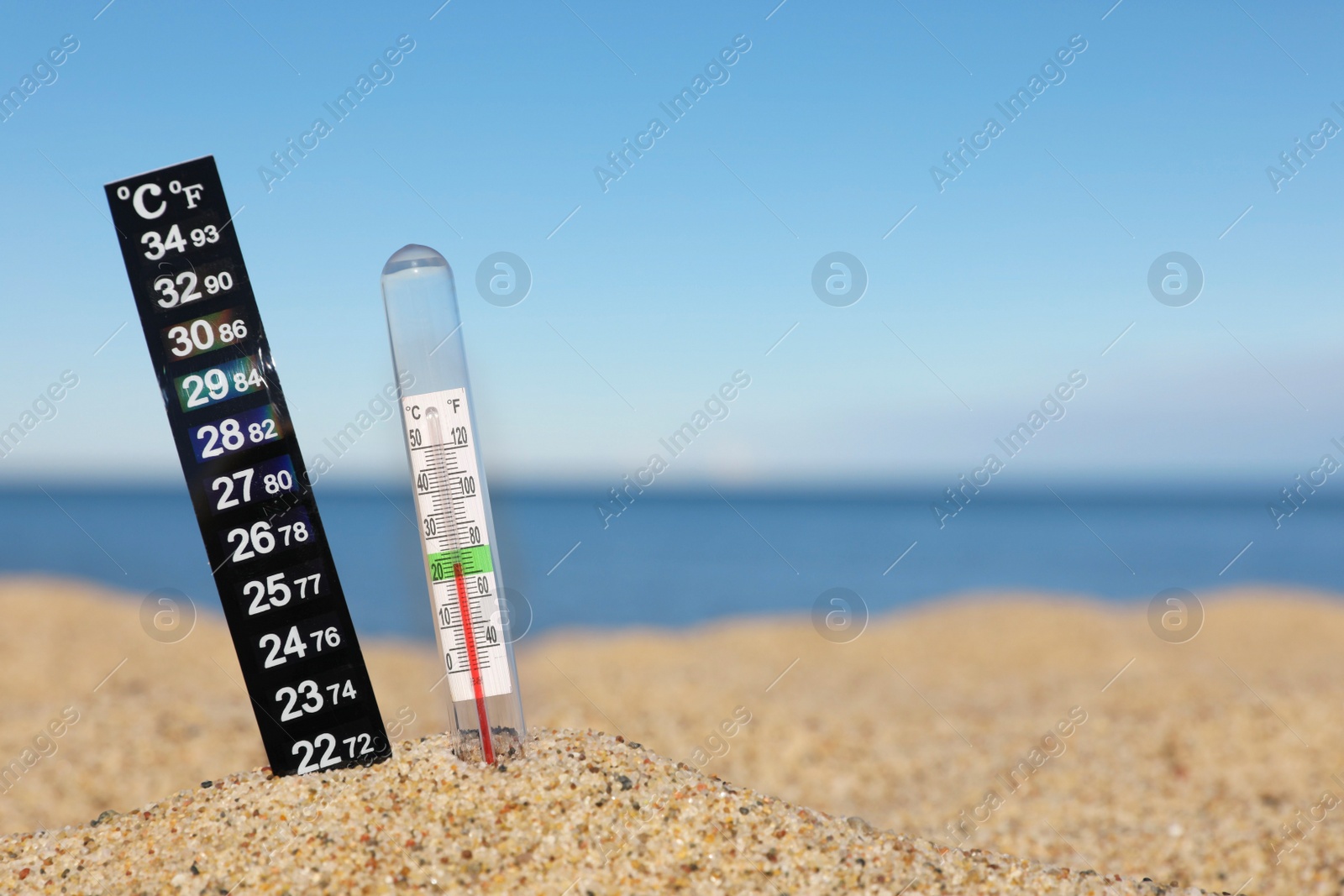 Photo of Weather thermometers in sand near sea, space for text