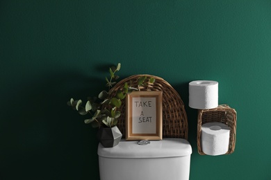 Decor elements, paper rolls and toilet bowl near green wall. Bathroom interior