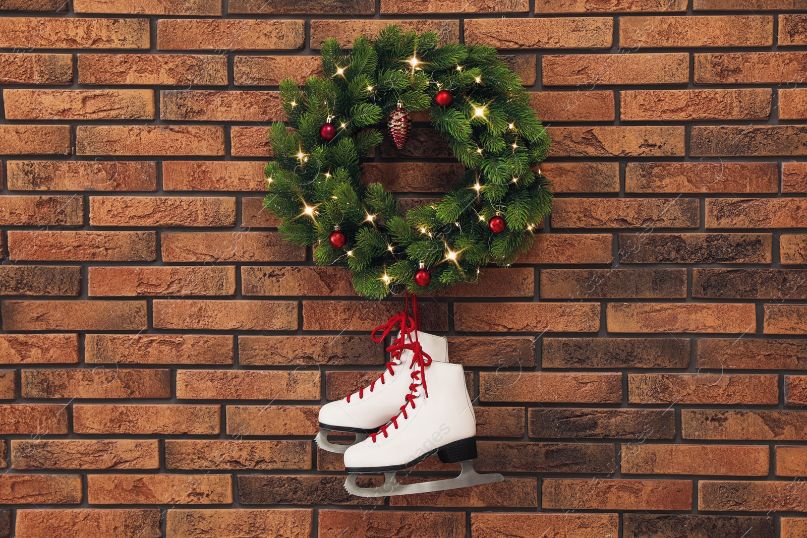 Photo of Pair of ice skates and beautiful Christmas wreath hanging on brick wall