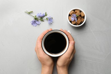 Woman holding cup of delicious chicory drink at light grey table, top view