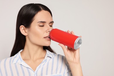 Photo of Beautiful young woman drinking from tin can on light grey background