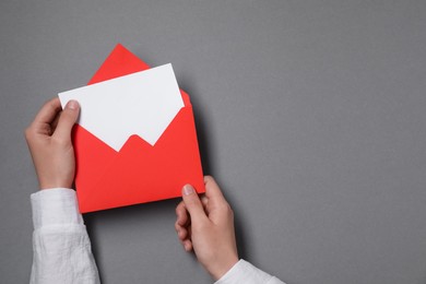 Photo of Woman taking card out of letter envelope at grey table, top view. Space for text