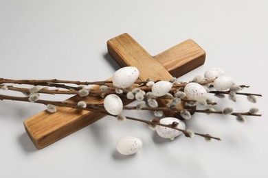 Wooden cross, painted Easter eggs and willow branches on light grey background