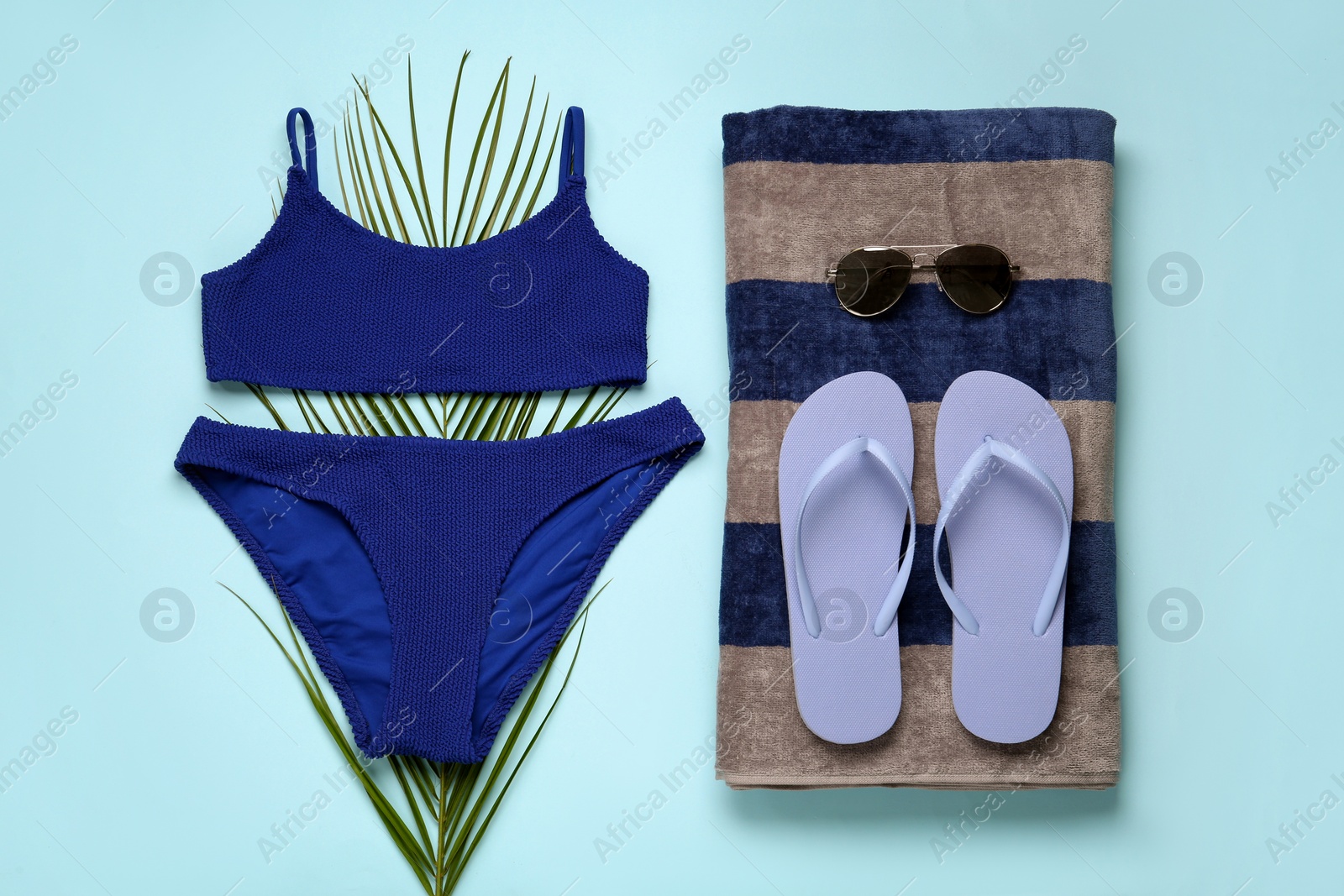 Photo of Beach towel, swimsuit, flip flops and sunglasses on light blue background, flat lay