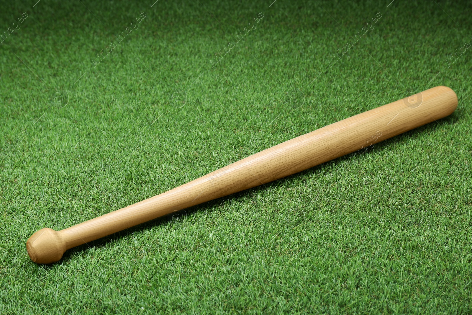 Photo of Wooden baseball bat on green grass, above view. Sports equipment