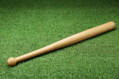 Photo of Wooden baseball bat on green grass, above view. Sports equipment