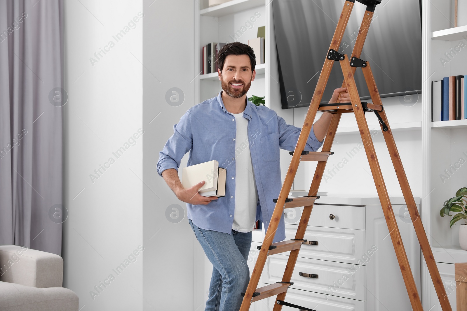 Photo of Happy man with books on wooden folding ladder at home