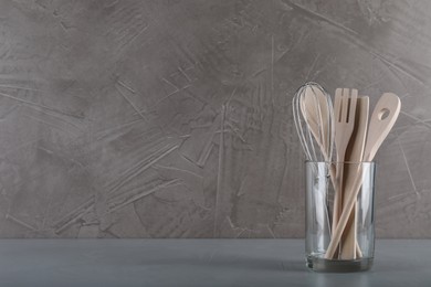 Photo of Holder with wooden kitchen utensils on grey table. Space for text