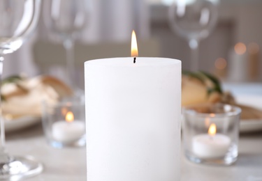 Photo of White burning wax candle on table, closeup