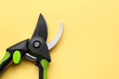Photo of Secateur on light yellow background, top view. Space for text