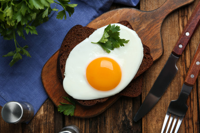 Photo of Tasty fried egg with parsley and rye bread on wooden table, flat lay