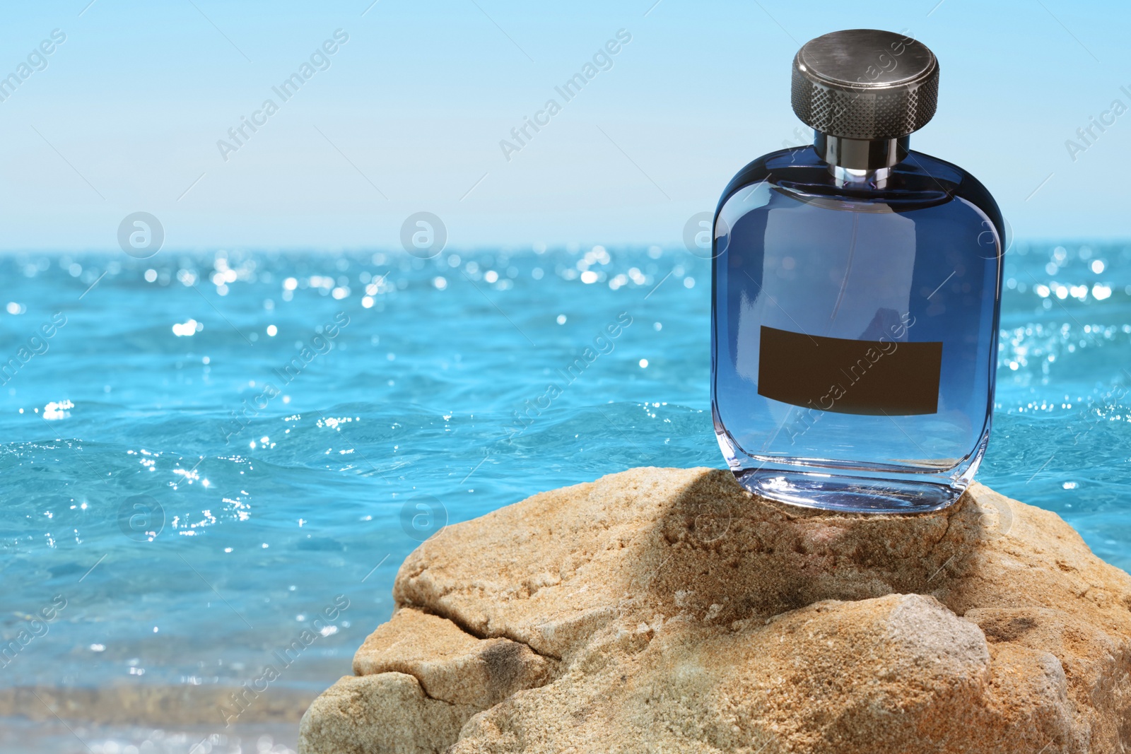 Image of Bottle of aquatic perfume on rock near ocean. Fresh sea breeze scent