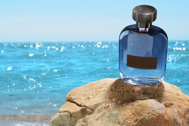 Bottle of aquatic perfume on rock near ocean. Fresh sea breeze scent