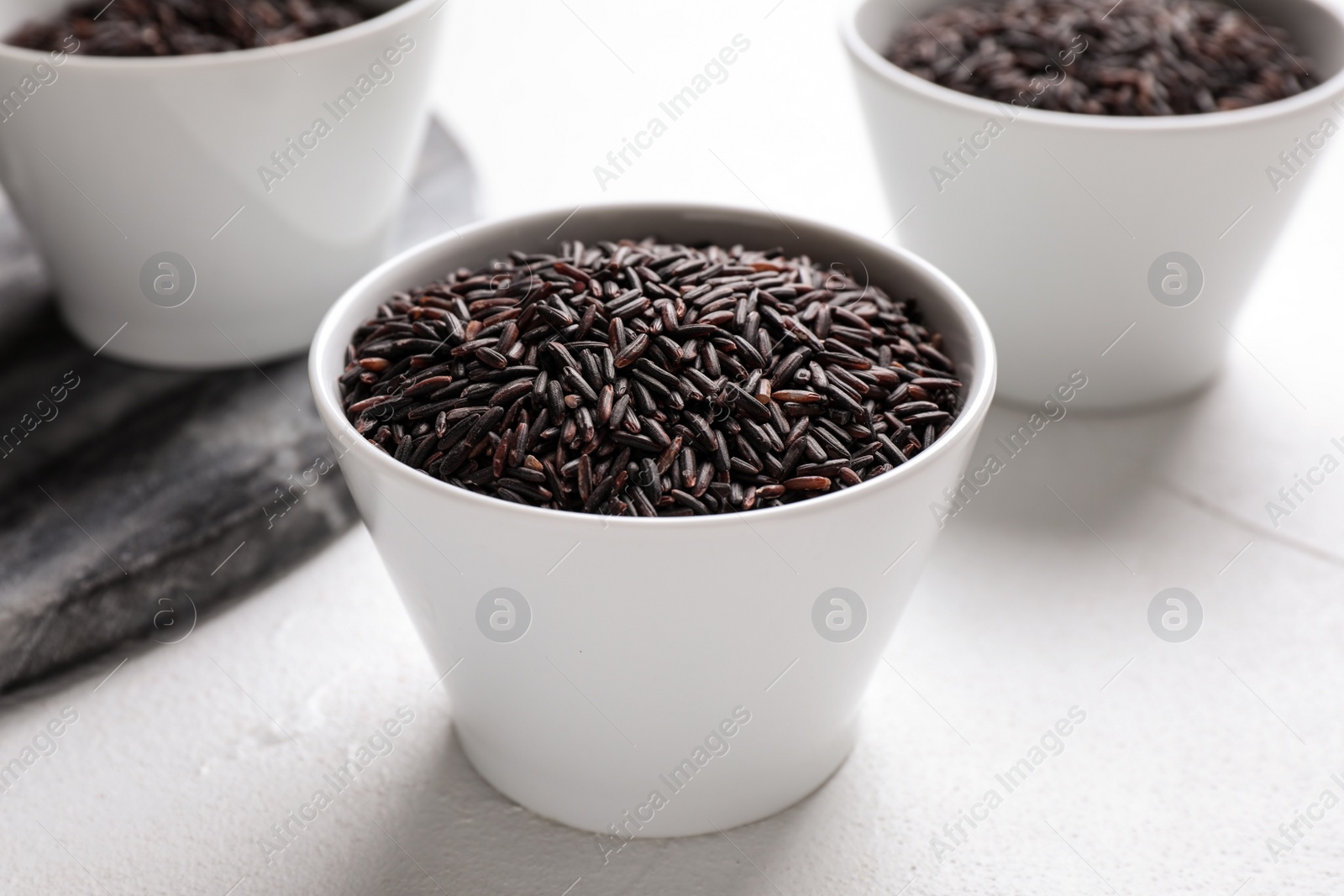 Photo of Uncooked brown rice in bowl on white table, closeup