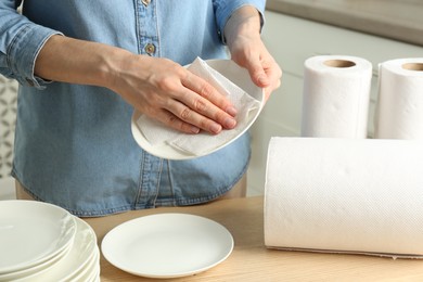 Photo of Woman wiping ceramic plate with paper towel indoors, closeup
