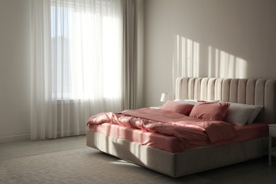 Photo of Comfortable bed with pink linens near beige wall