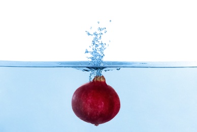 Pomegranate falling down into clear water against white background