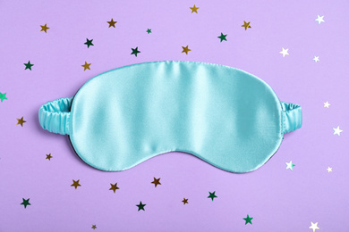 Photo of Sleeping mask and glitter on violet background, flat lay. Bedtime accessory
