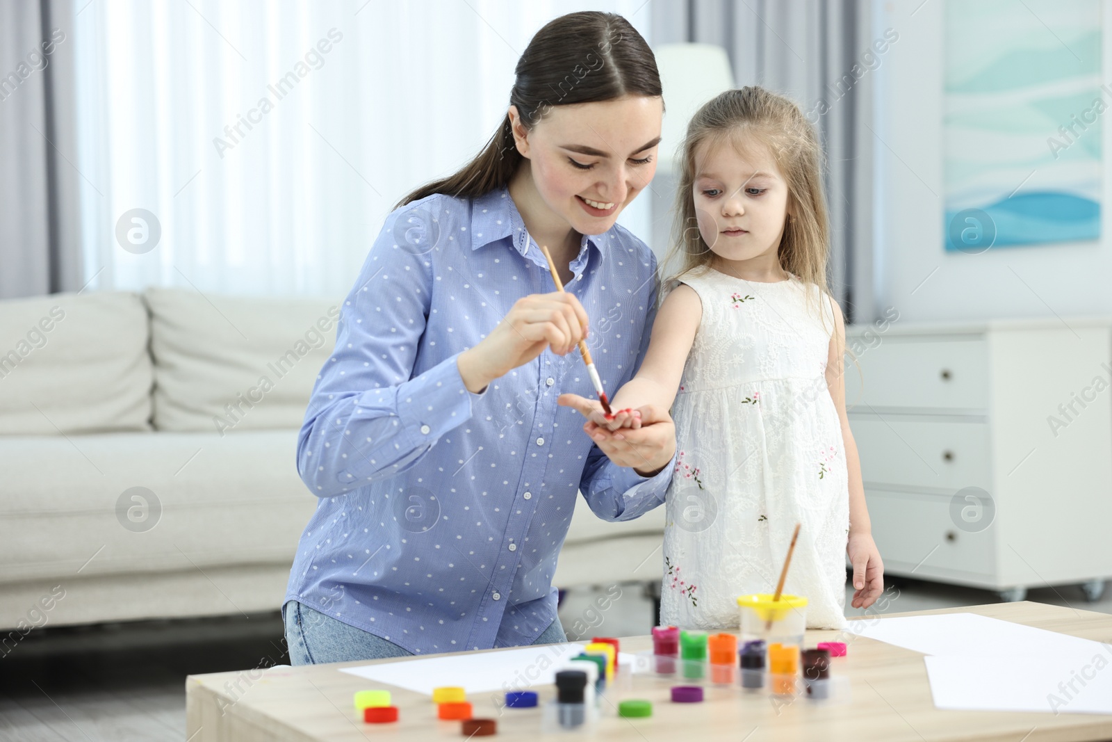 Photo of Mother and her little daughter painting with palms at home