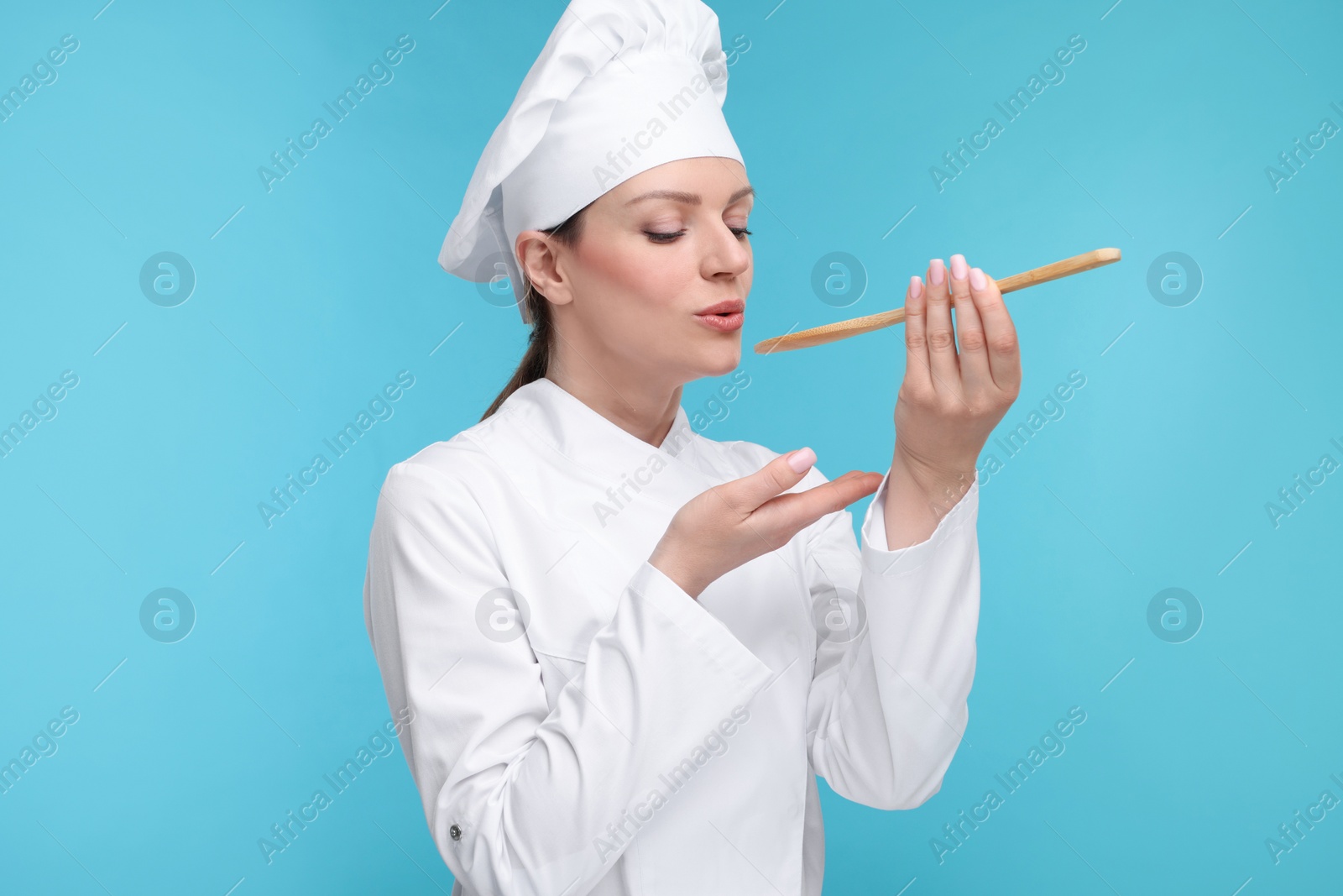 Photo of Woman chef in uniform tasting something on light blue background