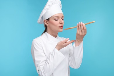 Photo of Woman chef in uniform tasting something on light blue background