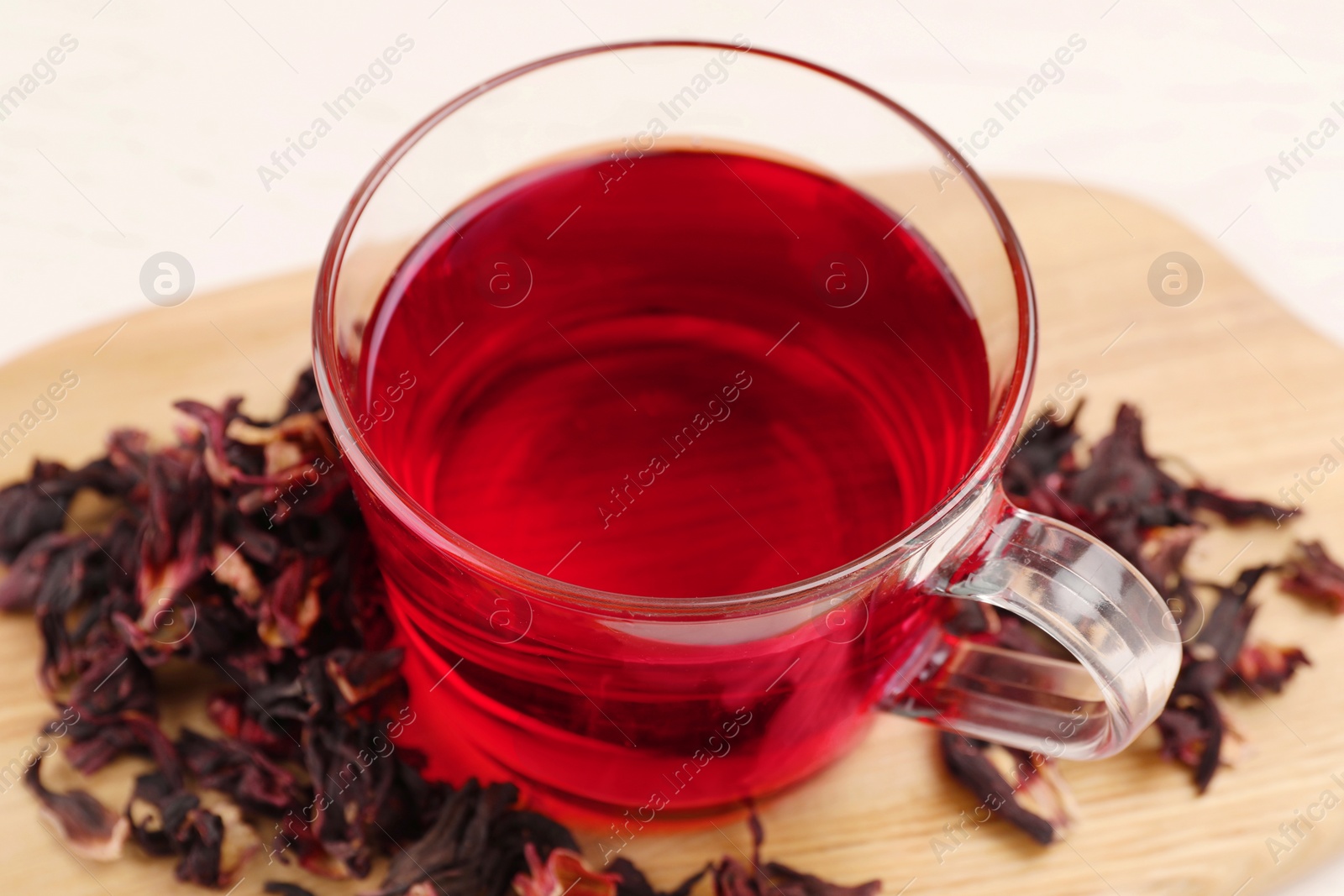 Photo of Cup of fresh hibiscus tea and dry flower leaves on wooden table, closeup