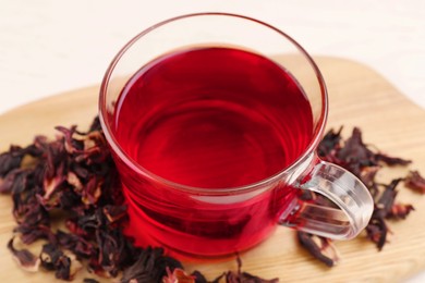 Cup of fresh hibiscus tea and dry flower leaves on wooden table, closeup