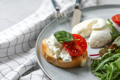 Delicious burrata cheese with tomatoes, arugula and toast on checkered tablecloth, closeup
