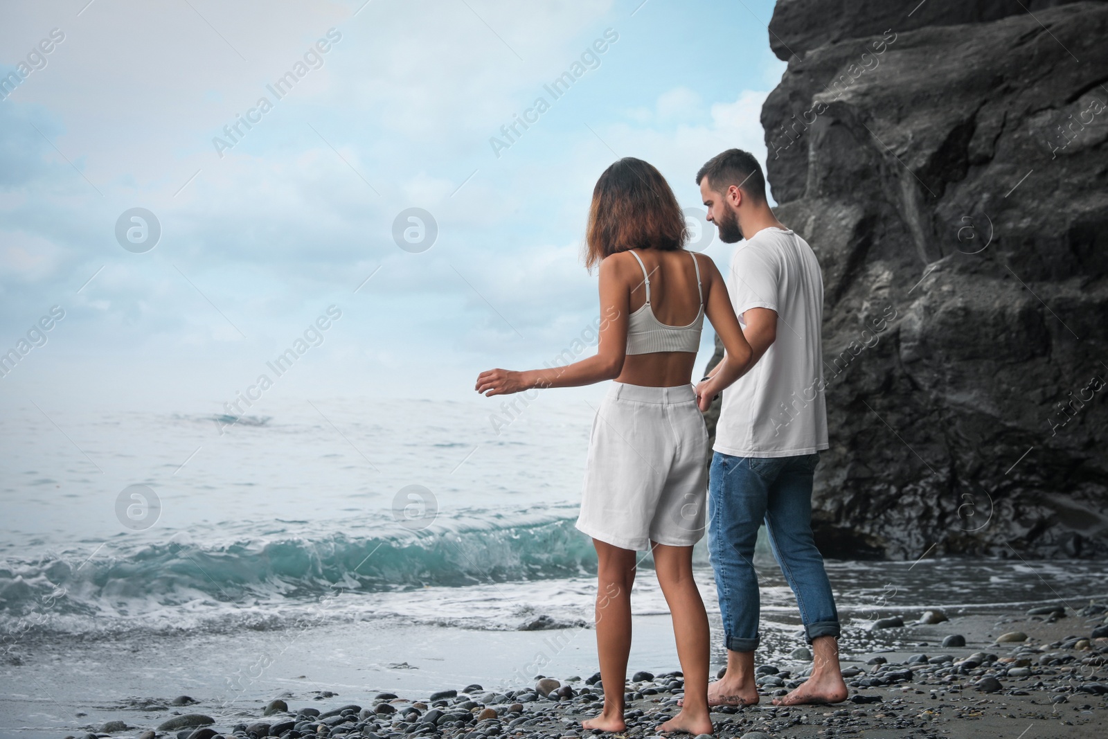 Photo of Young couple walking on beach near sea. Space for text