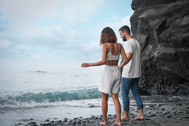 Photo of Young couple walking on beach near sea. Space for text
